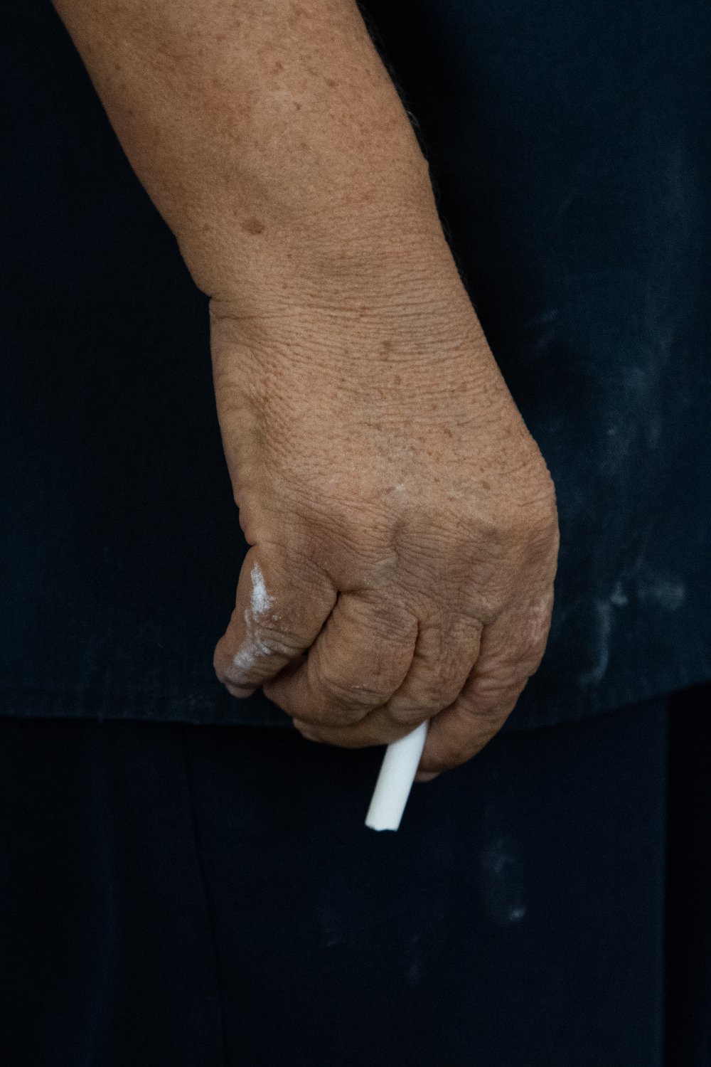Detalle de la mano de Julio. Su ropa negra y las manchas por la tiza como casi todos los días desde que comenzó a dar clases en el IPVCE en el 86.